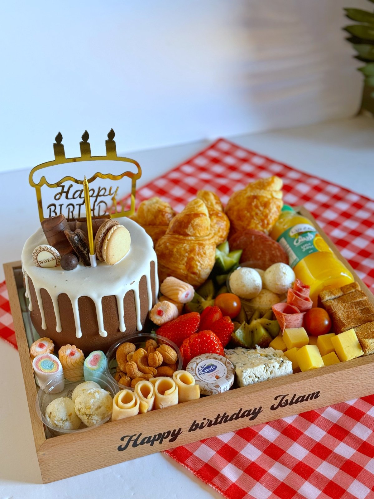 A full view of the birthday tray with a variety of treats, including croissants, fruits, cheese, and cake, customized with a "Happy Birthday Islam" wooden engraving.