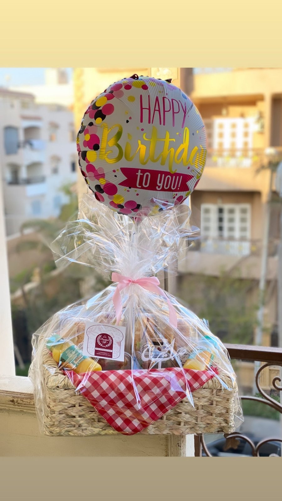 A full view of the Breakfast for Two People basket, featuring sandwiches, fresh vegetables, chocolates, a "صباح الخير" topper, and a birthday balloon in the background, elegantly wrapped for a special morning meal.