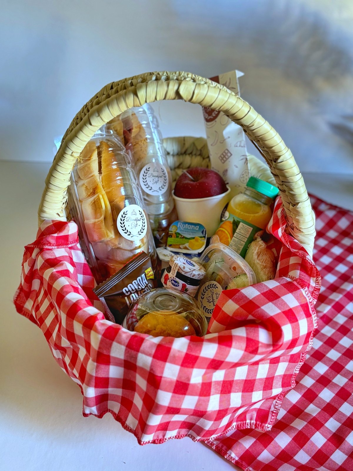 Breakfast with Sandwiches gift basket, featuring a wicker tray with cheddar cheese and smoked turkey sandwich, roast beef sandwich, toast, a muffin cake, fresh fruit, tomatoes, cucumbers, natural juice, tea, Hero jam, Lurpak butter, and a Coco Lovers biscuit. A delightful breakfast experience in an elegant woven basket.