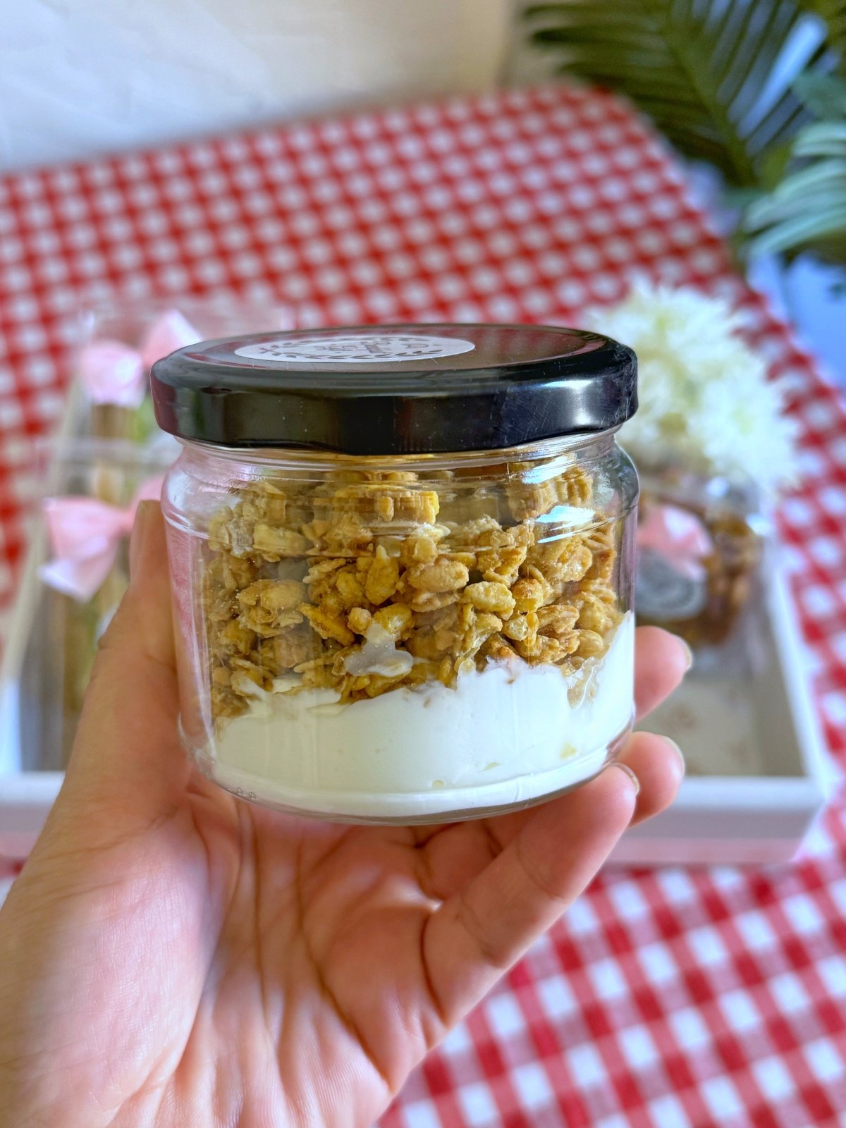 A close-up view of a glass jar filled with Greek yogurt topped with crunchy granola, showcasing a healthy and delicious addition to the breakfast tray.