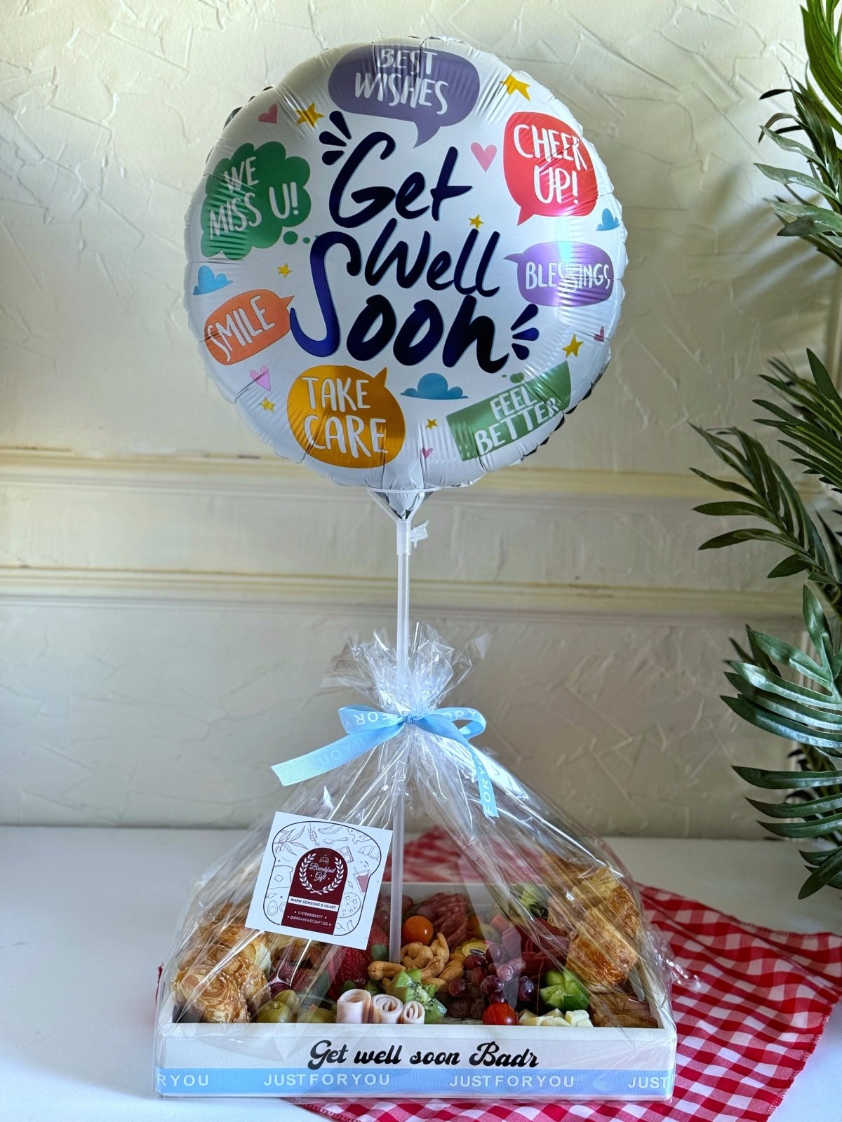 A beautifully packaged breakfast gift tray wrapped in transparent film with a decorative ribbon, featuring a heartfelt gift tag and a festive balloon.