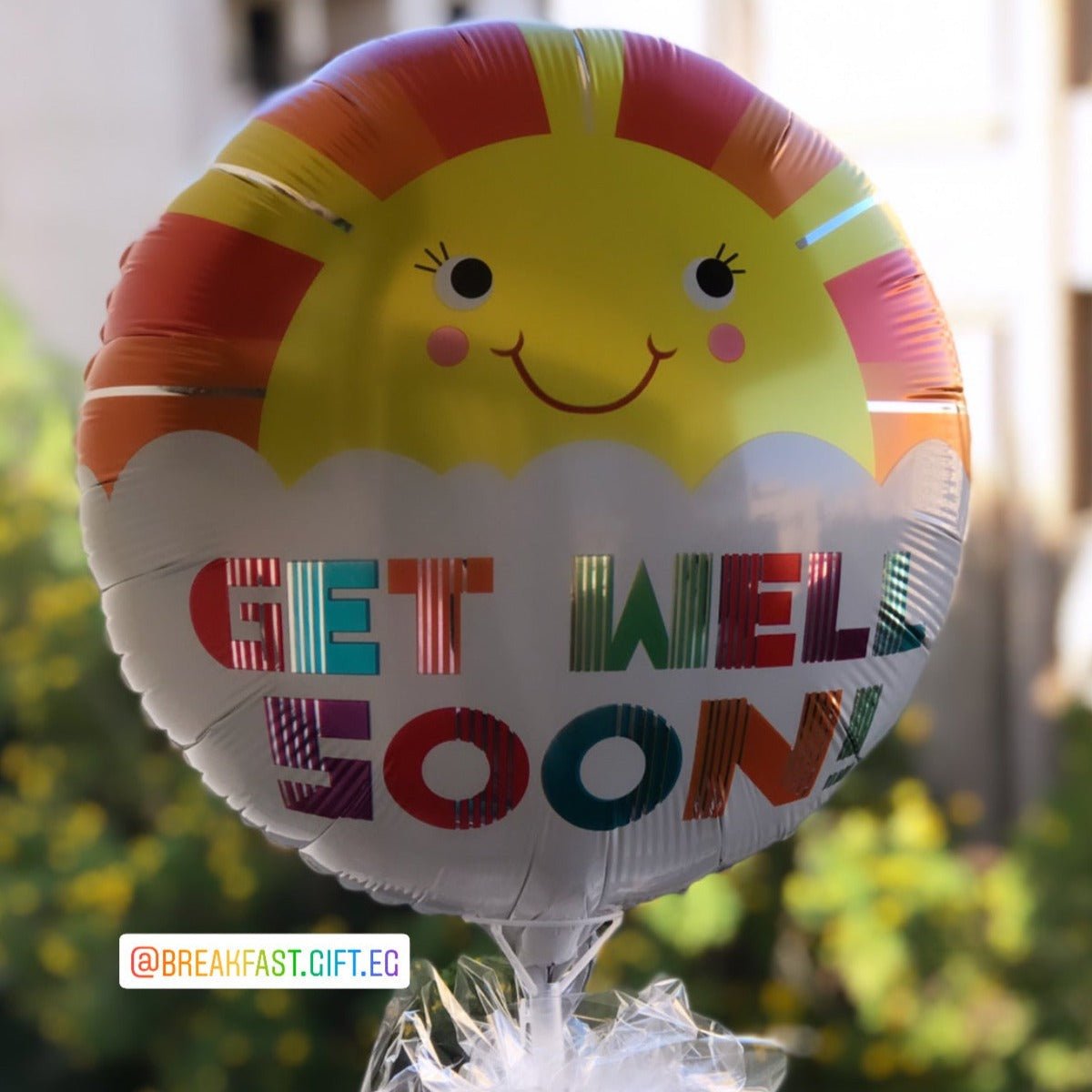 A vibrant Get Well Soon balloon featuring a bold yellow center with colorful geometric patterns and multicolored text, tied to a wrapped gift for a cheerful recovery surprise.