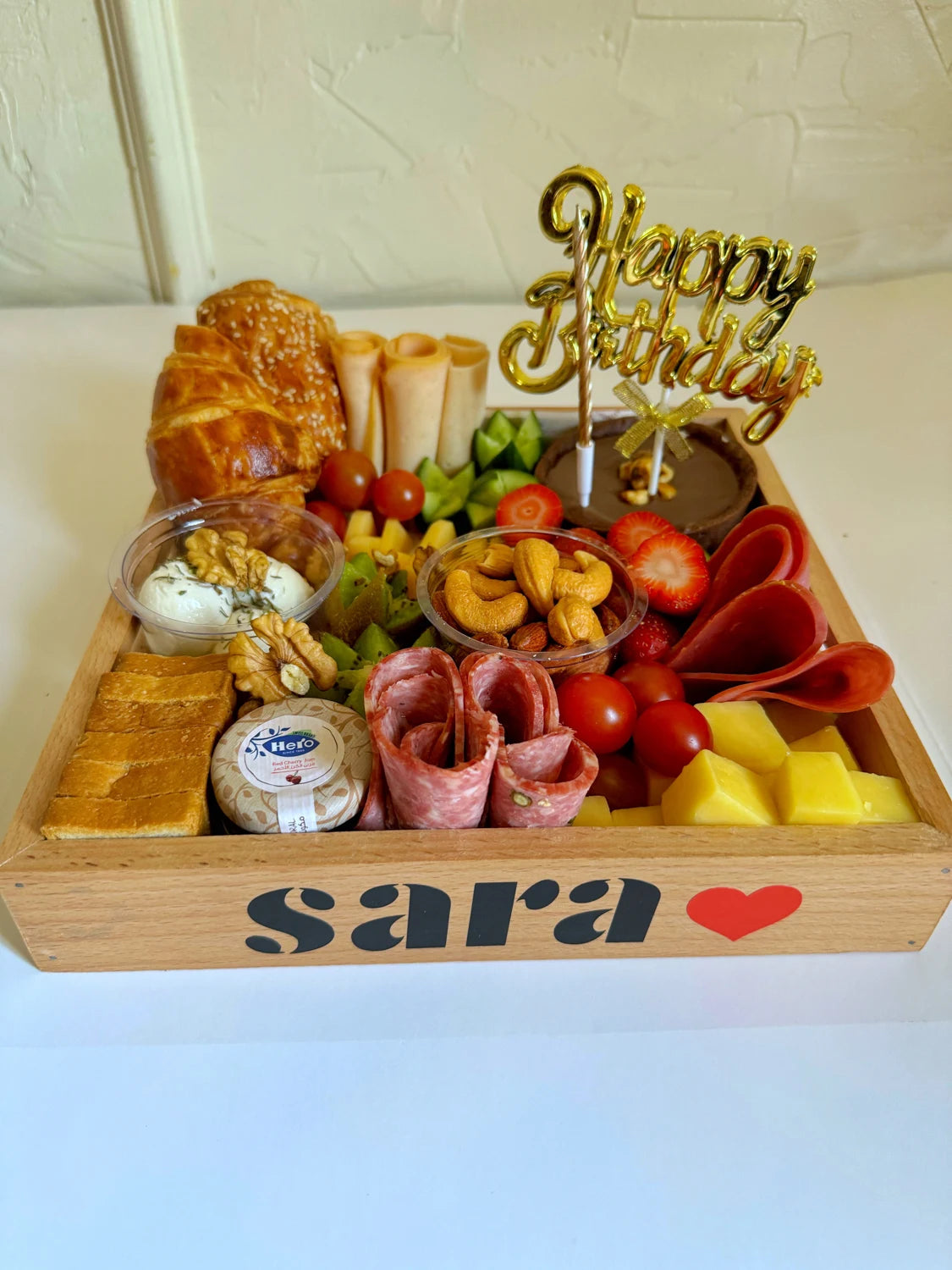 A personalized birthday breakfast tray with mini chocolate cake, fruits, turkey rolls, and mixed snacks.