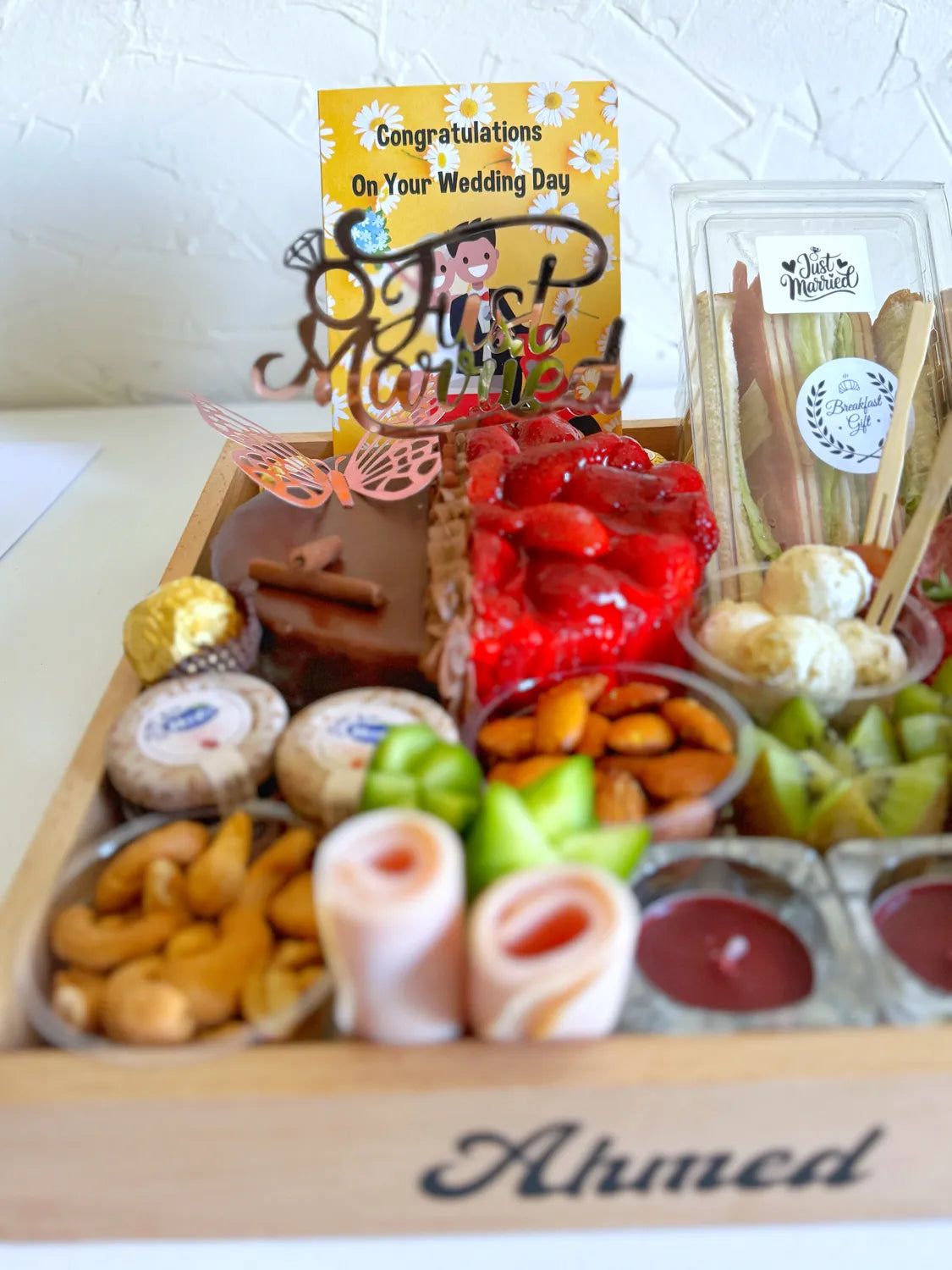 Close-up of the wooden tray with personalized names, candles, cheese cubes, and a vibrant mix of breakfast items.