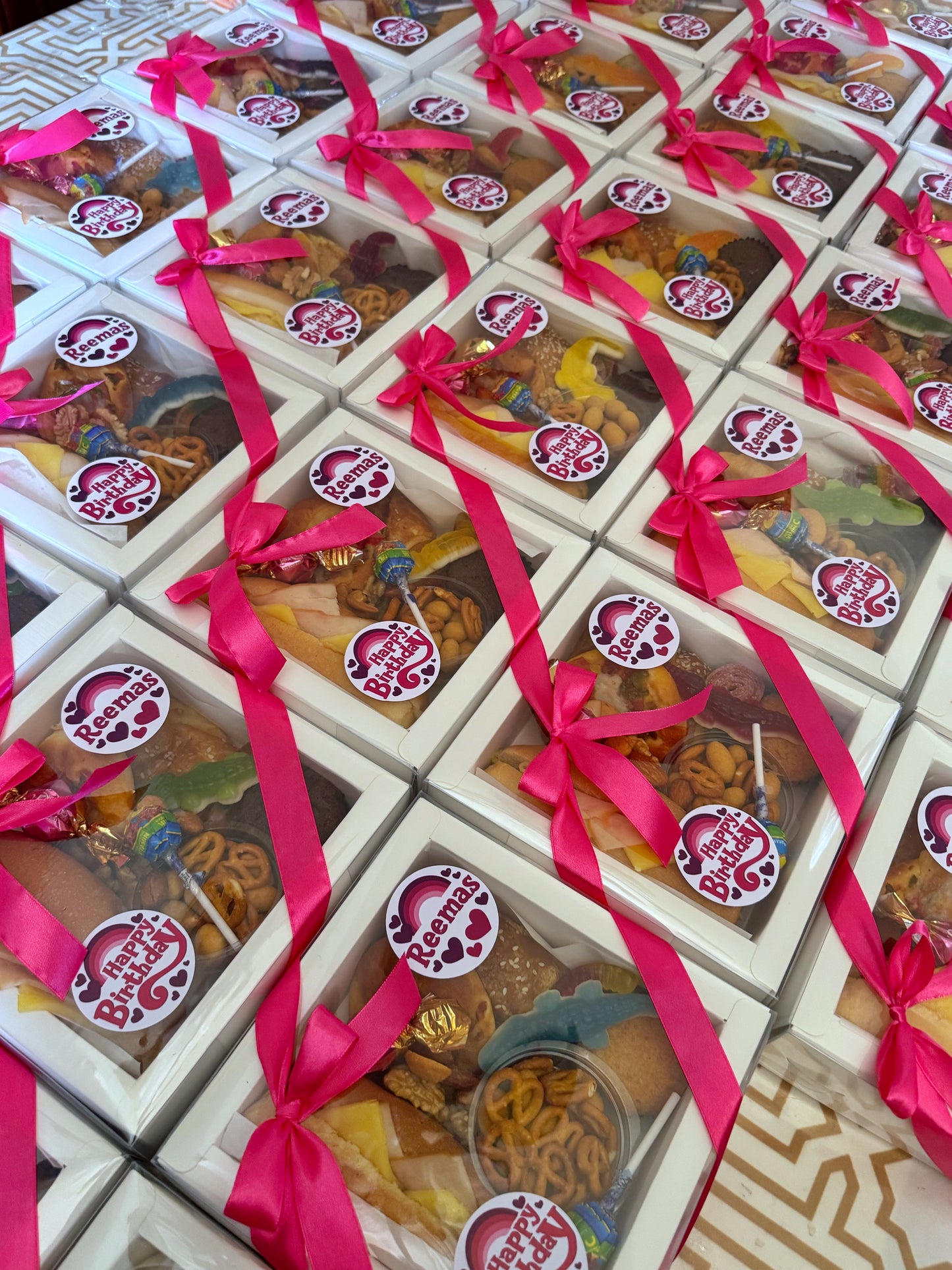 Multiple closed Mini Bites Birthday Boxes arranged in rows, each with pink ribbon and a custom birthday sticker.