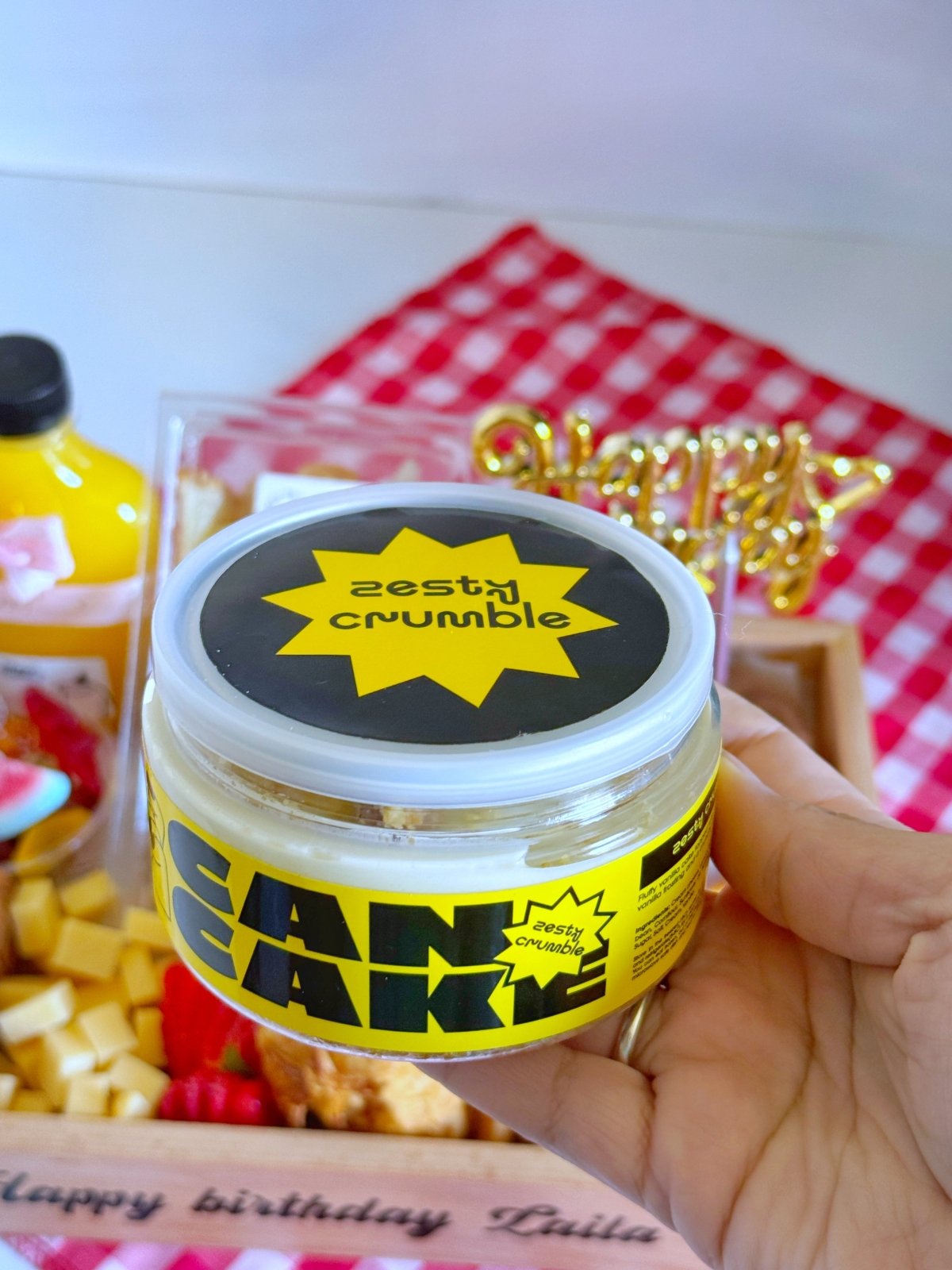 Hand holding a zesty crumble canned cake jar with bold yellow and black packaging, perfectly matching the trendy birthday breakfast theme.