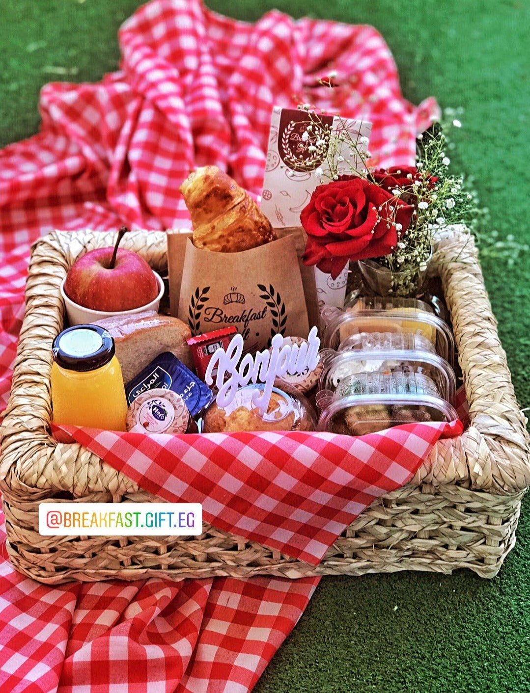 Breakfast Basket & Vase Flowers gift set, featuring a wicker tray with a flaky croissant, toast, muffin cake, fresh fruit, natural juice, cheese, honey, jam, Kit Kat chocolate, and a 'Bonjour' topper. Includes a vase of fresh red flowers for a beautiful and thoughtful morning surprise.