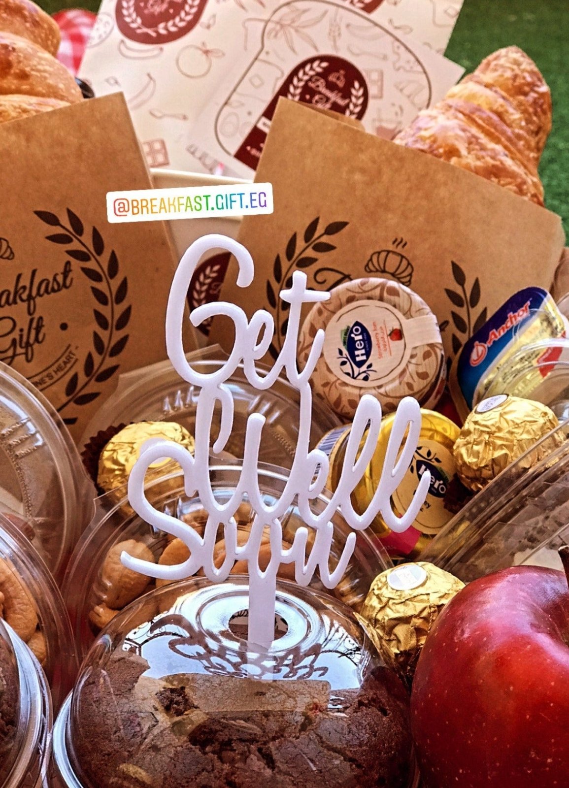 Close-up of the Get Well Soon Breakfast gift basket, featuring a 'Get Well Soon' topper, croissants, muffins, chocolates, honey, jam, nuts, and dairy products. A thoughtful breakfast gift to bring comfort and care.