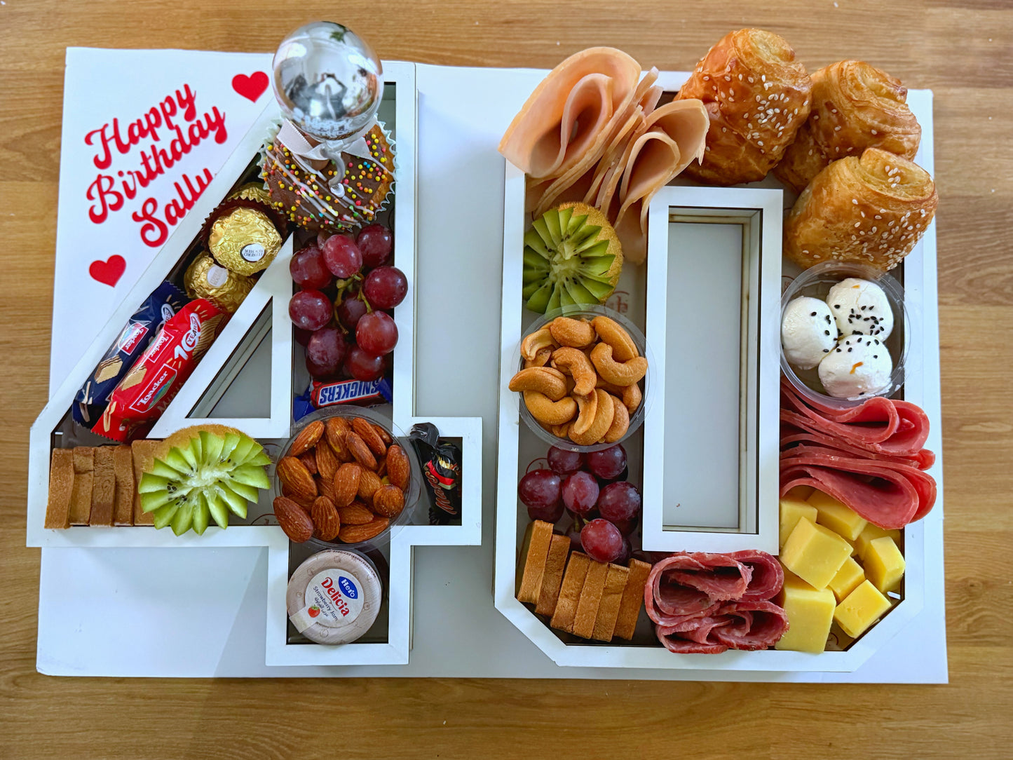 Birthday gift box with assorted foods shaped like the number 40 on a wooden surface.