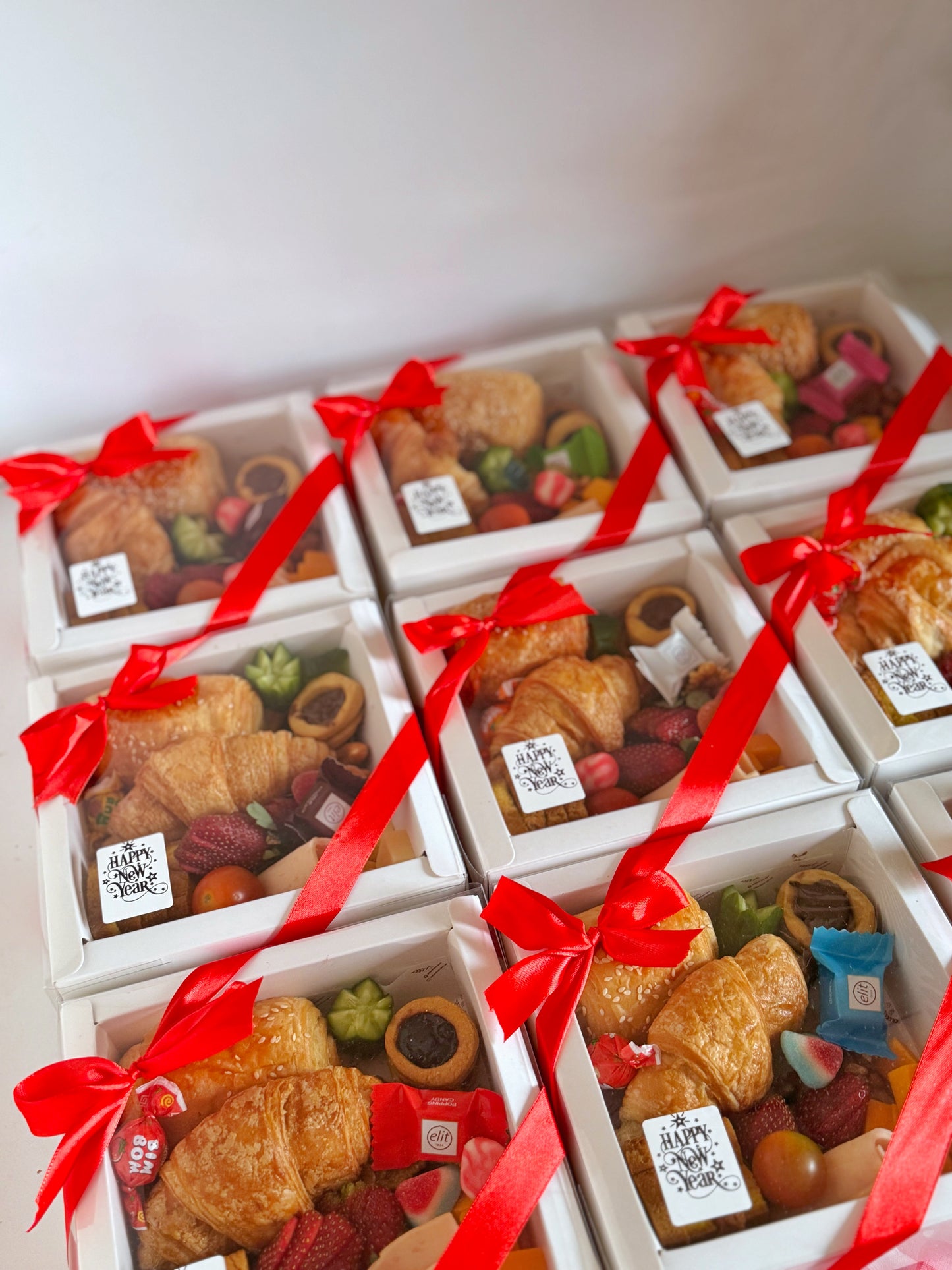 A neatly wrapped Corporate Gift Box with a red ribbon, showcasing an elegant selection of breakfast pastries, cheeses, fresh strawberries, cucumber slices, cherry tomatoes, and chocolate treats, designed for corporate celebrations.