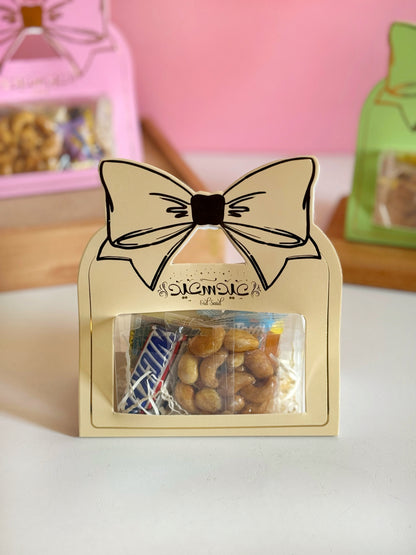 A yellow Eid Bow Gift Box with a clear window, revealing chocolates, caramel candies, and nuts, perfect for Eid gifting.