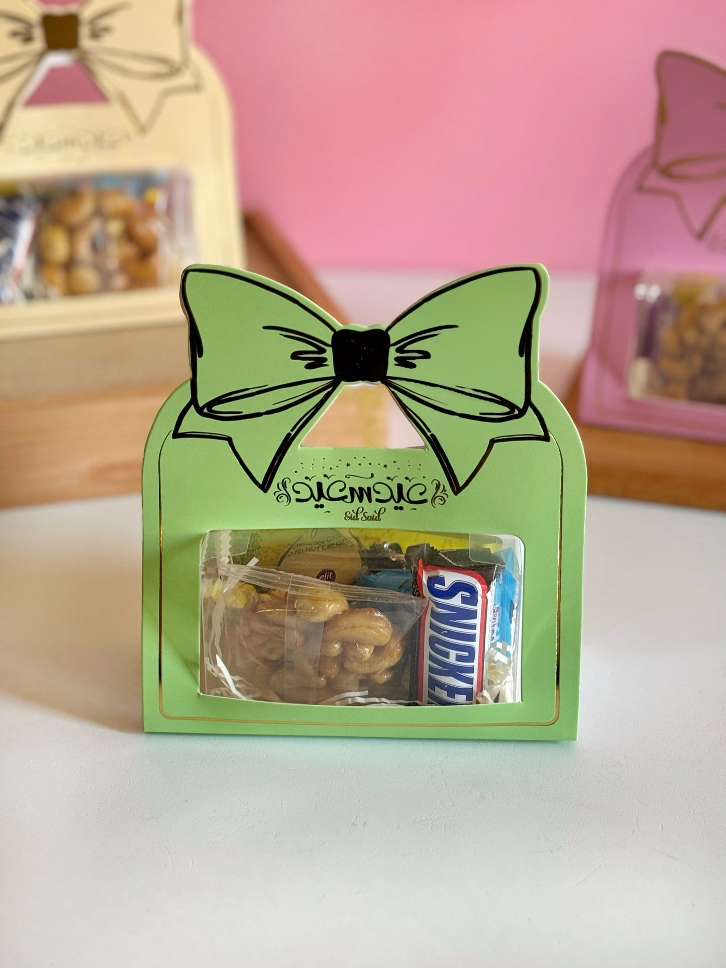 A green Eid Bow Gift Box filled with assorted treats, showcasing its premium design with a bow-shaped handle.