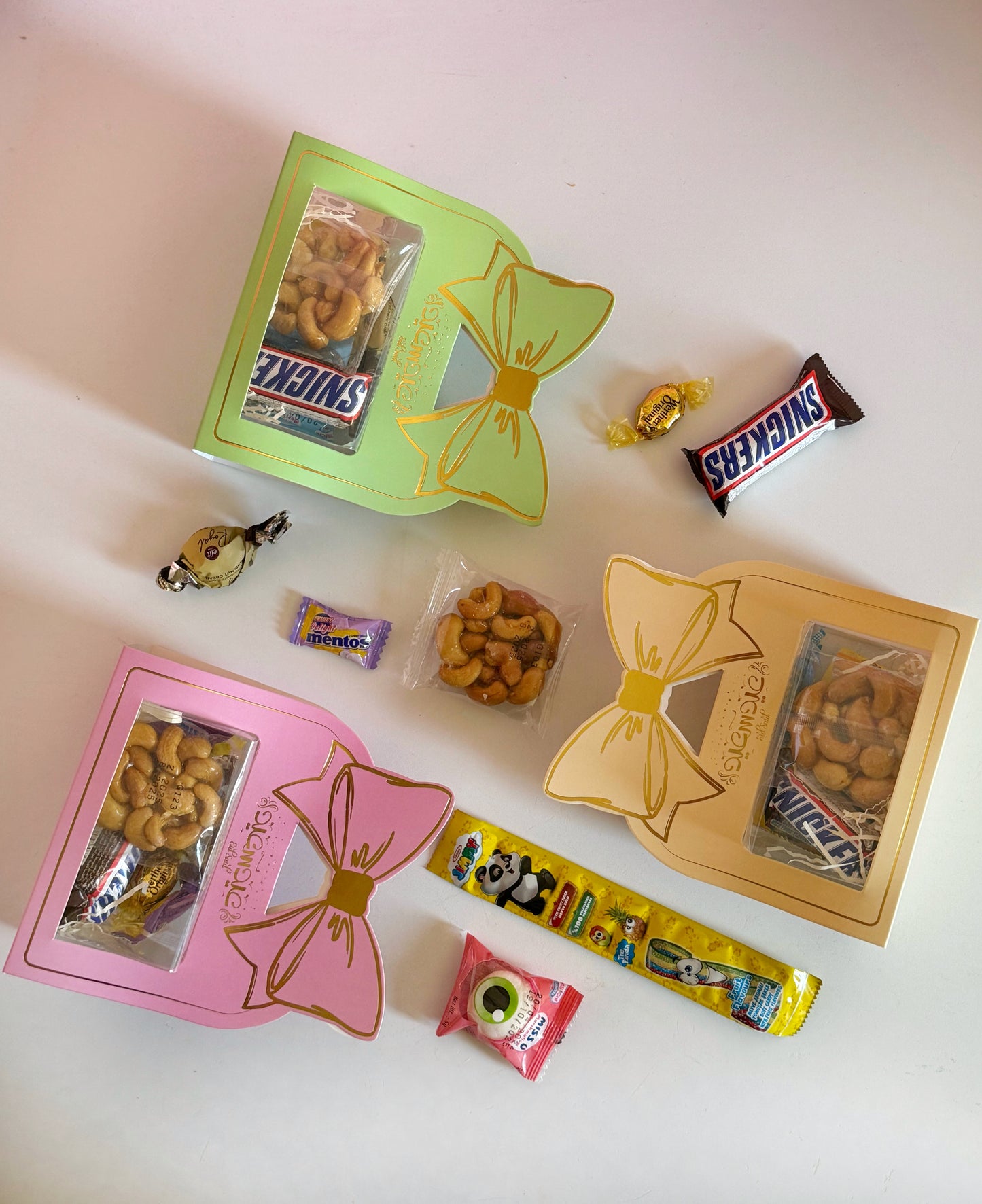 An open Eid Bow Gift Box displaying its delicious contents, including Snickers, Mentos, caramel chocolates, and sugared cashews.