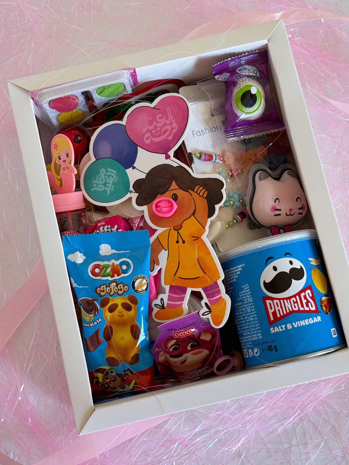 A top view of the Eid Festive Surprise - Girl gift box, featuring candy, jewelry, and coloring activities.