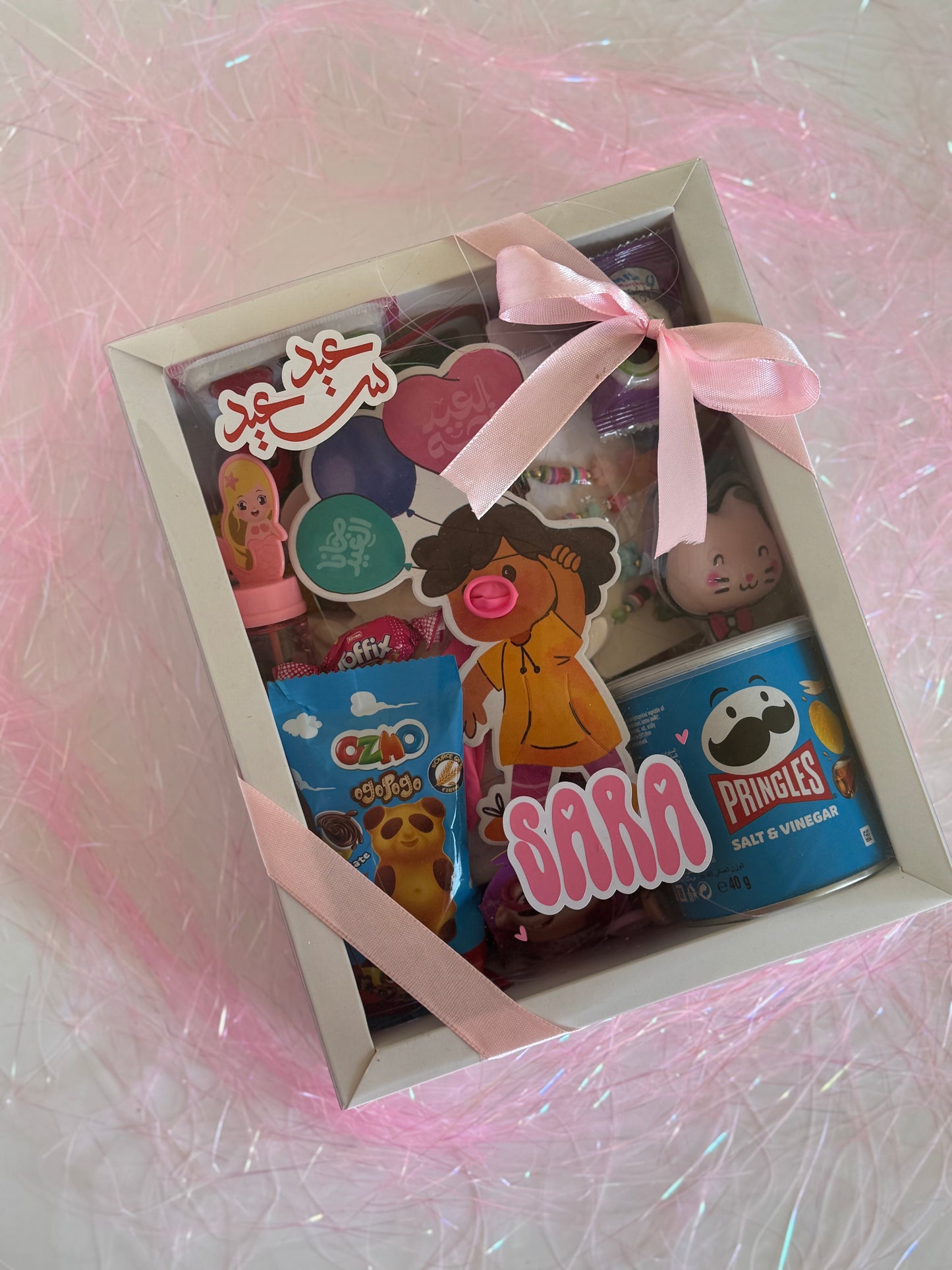 Eid Festive Surprise - Girl gift box with personalized name, sweets, and fun activities, decorated with a pink ribbon.