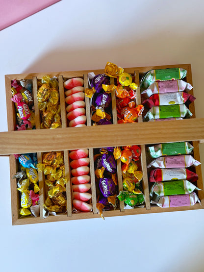 Top-down view of the Eid wooden tray showcasing colorful bonbons, caramel candies, Spanish jellies, and wrapped biscuits neatly arranged in compartments.