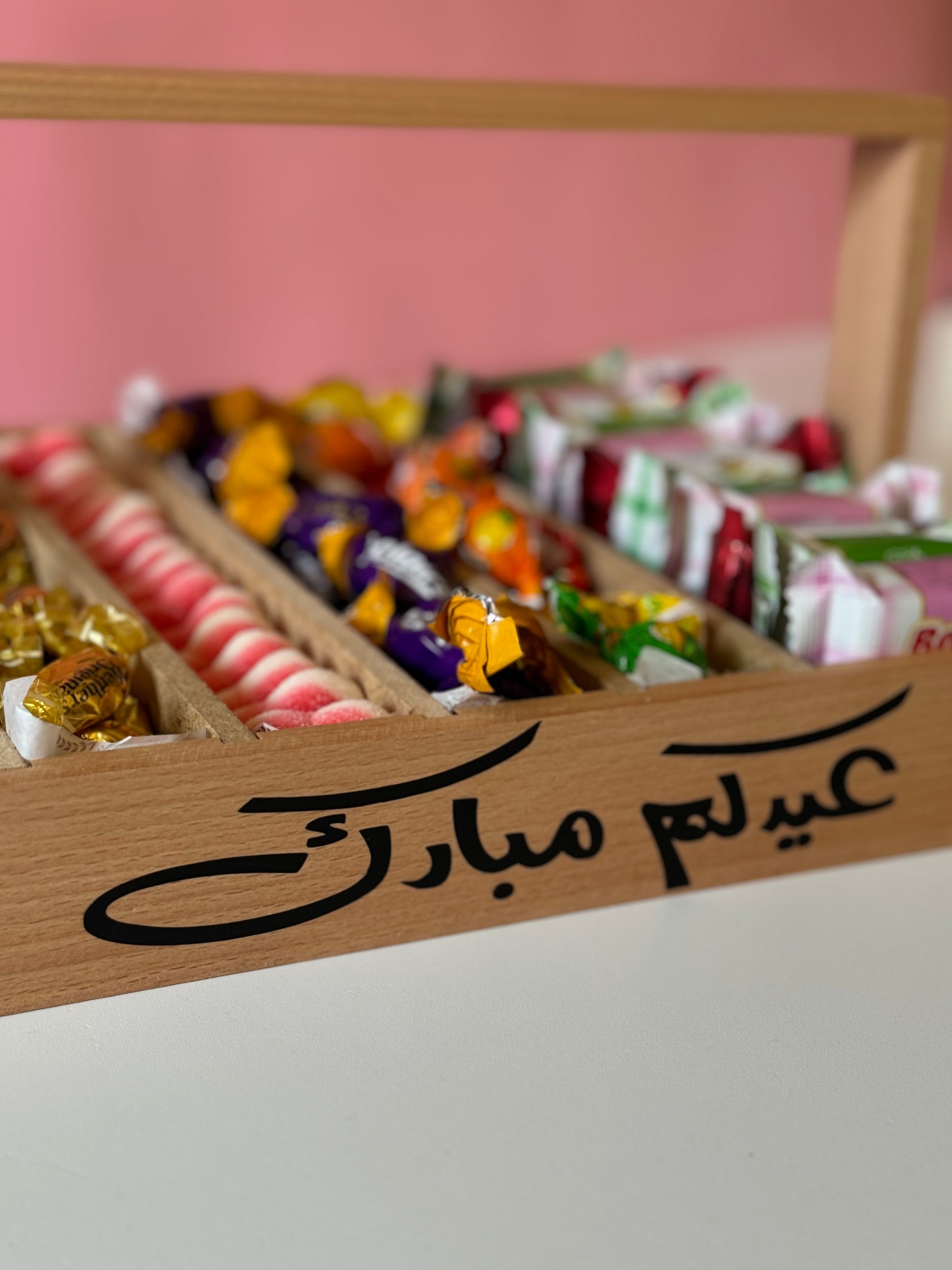 A close-up on the Eid-themed wooden tray with a festive background, featuring compartments filled with a variety of sweets and bonbons, perfect for family gatherings.