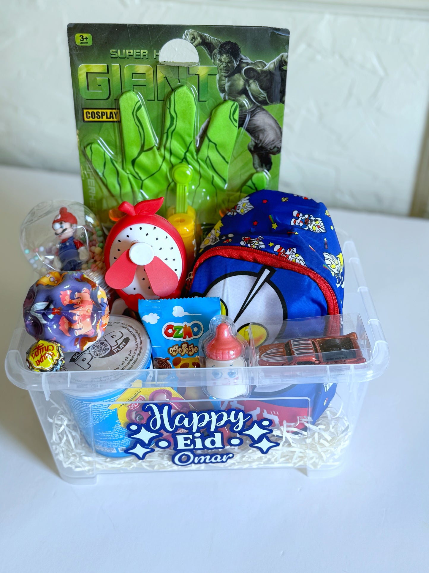 Eid Hero Box - Boy featuring a personalized printed box, superhero gloves, a mini car, bubbles, slime, Ozmo cake, and an assortment of Eid treats.