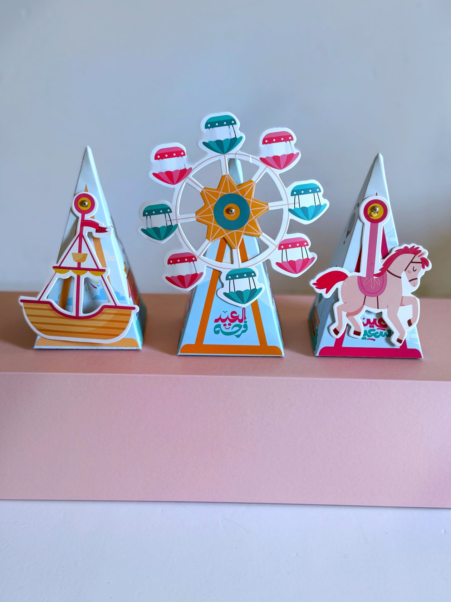 A Movable Eid Pyramid Set featuring three colorful pyramid designs with interactive moving parts—a carousel, a horse, and a boat—perfect for children's Eid celebrations.