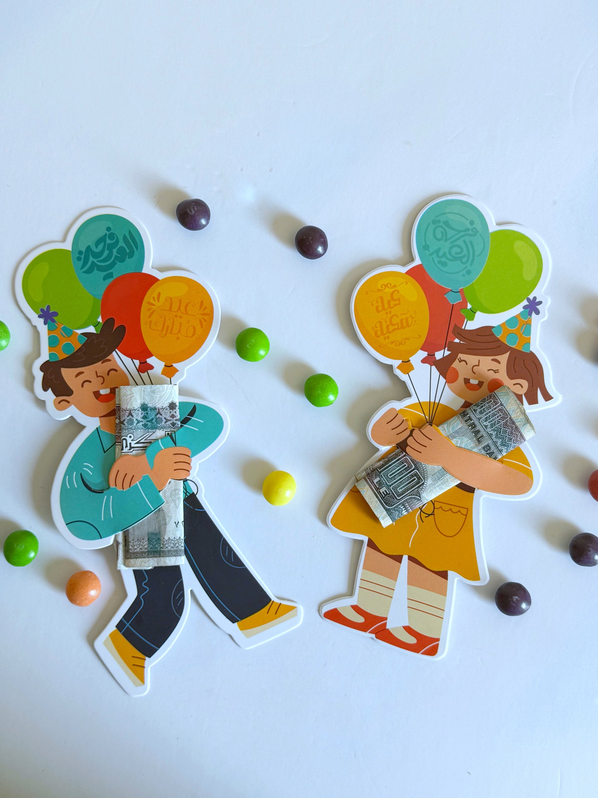 A set of two Eidiyya cards, one featuring a boy and the other a girl, both designed with balloons containing candies and a money holder for Eid gifting.