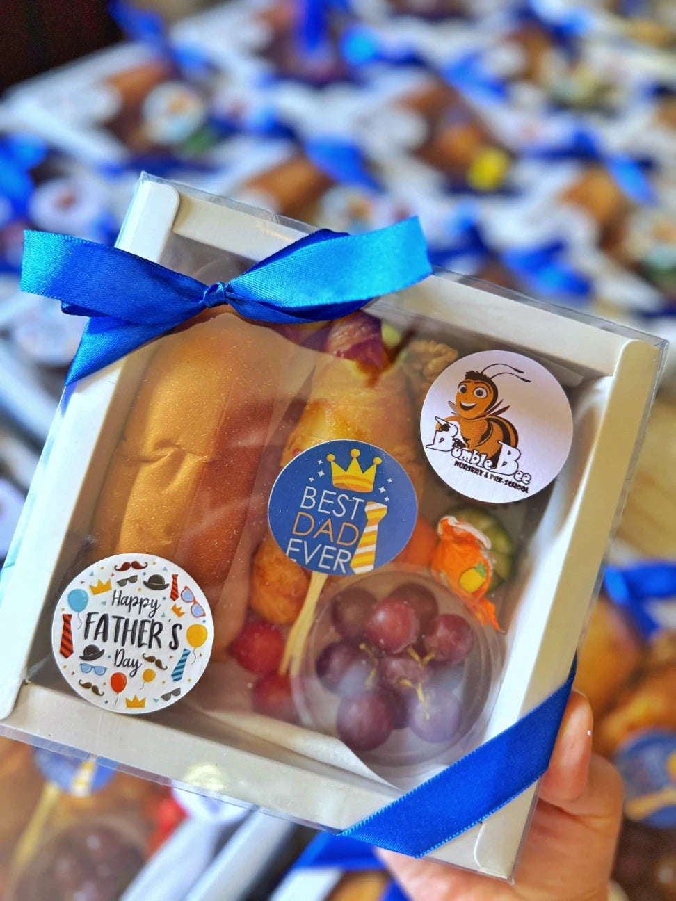 The closed Little Cheers Box, decorated with a custom sticker featuring a cartoon character and a festive ribbon for events.