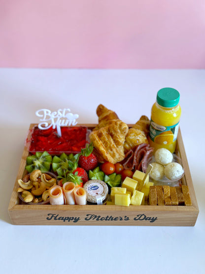 Elegant wooden Mother's Day breakfast tray with kunafa, croissants, cheese, nuts, fresh fruits, and a festive "Best Mom" topper.