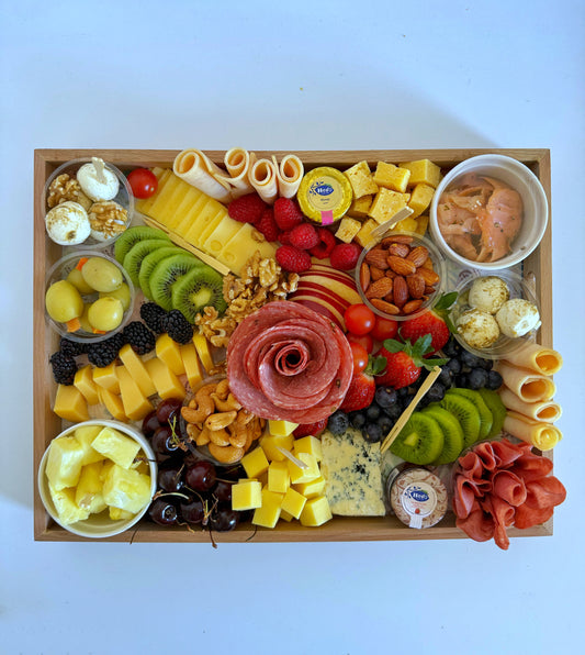 Overhead full view of the platter showing all contents: cheeses, cold cuts, fruits, nuts, salmon, and jam in an elegant wood tray.