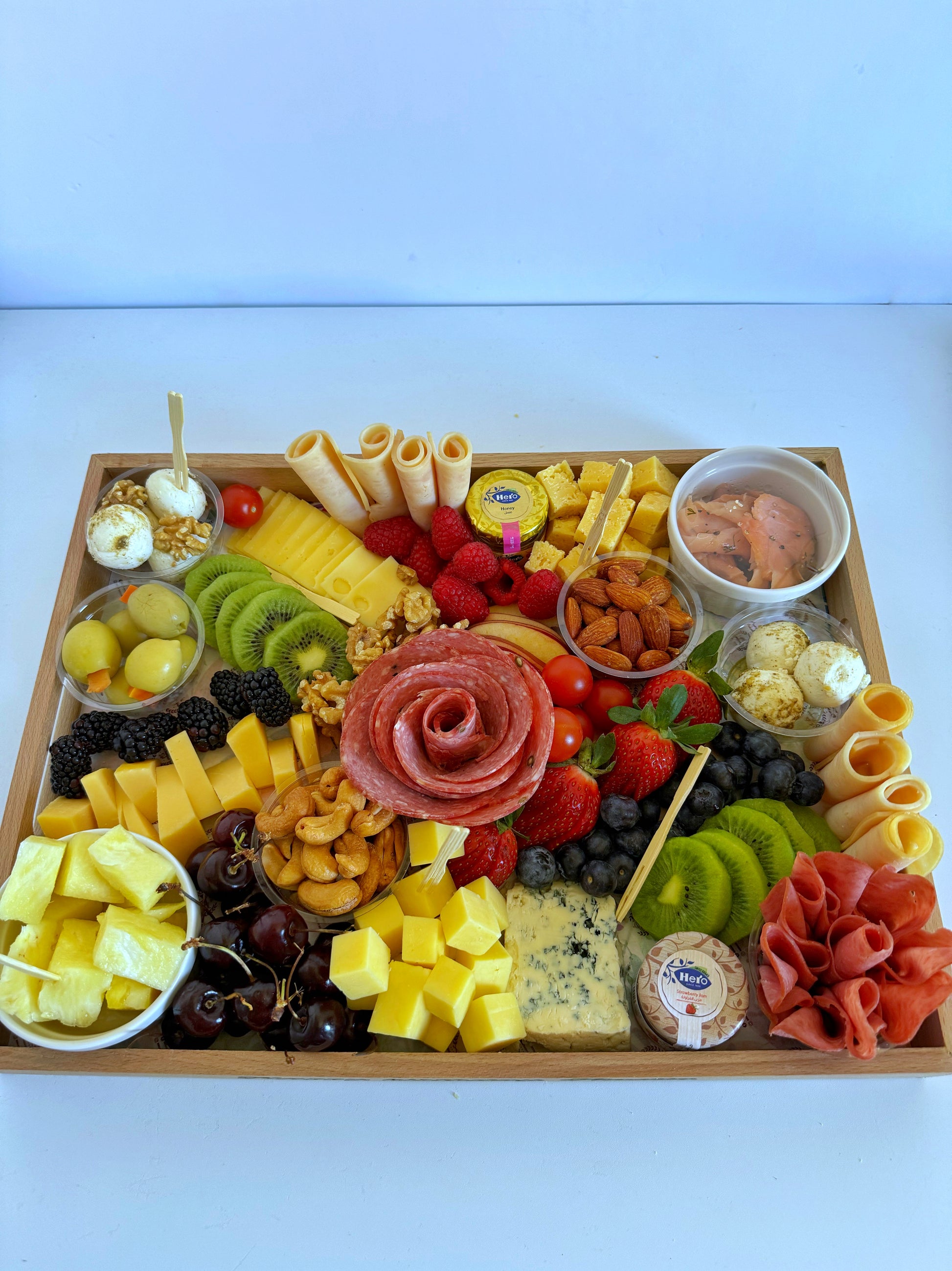 Top-down view of a premium 30×40 cheese and charcuterie platter with pineapple, cheddar, salami, olives, berries, and dips.