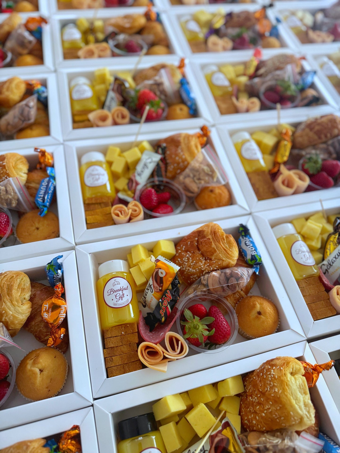 Premium Box – Overhead grid shot of multiple boxes packed with cheese, cold cuts, croissant, juice, and fruit
