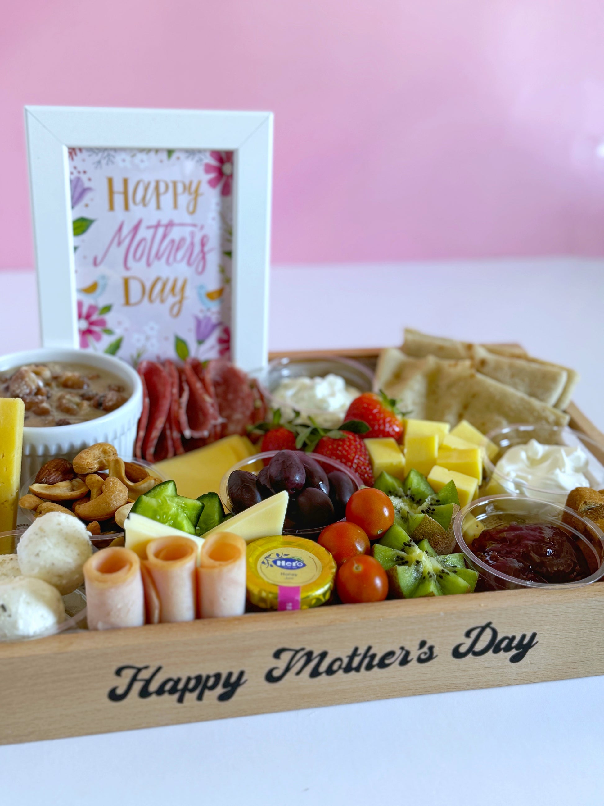 A wooden suhoor tray with a selection of premium cheeses, cold cuts, labneh, jam, and honey, arranged for a Mother's Day celebration.