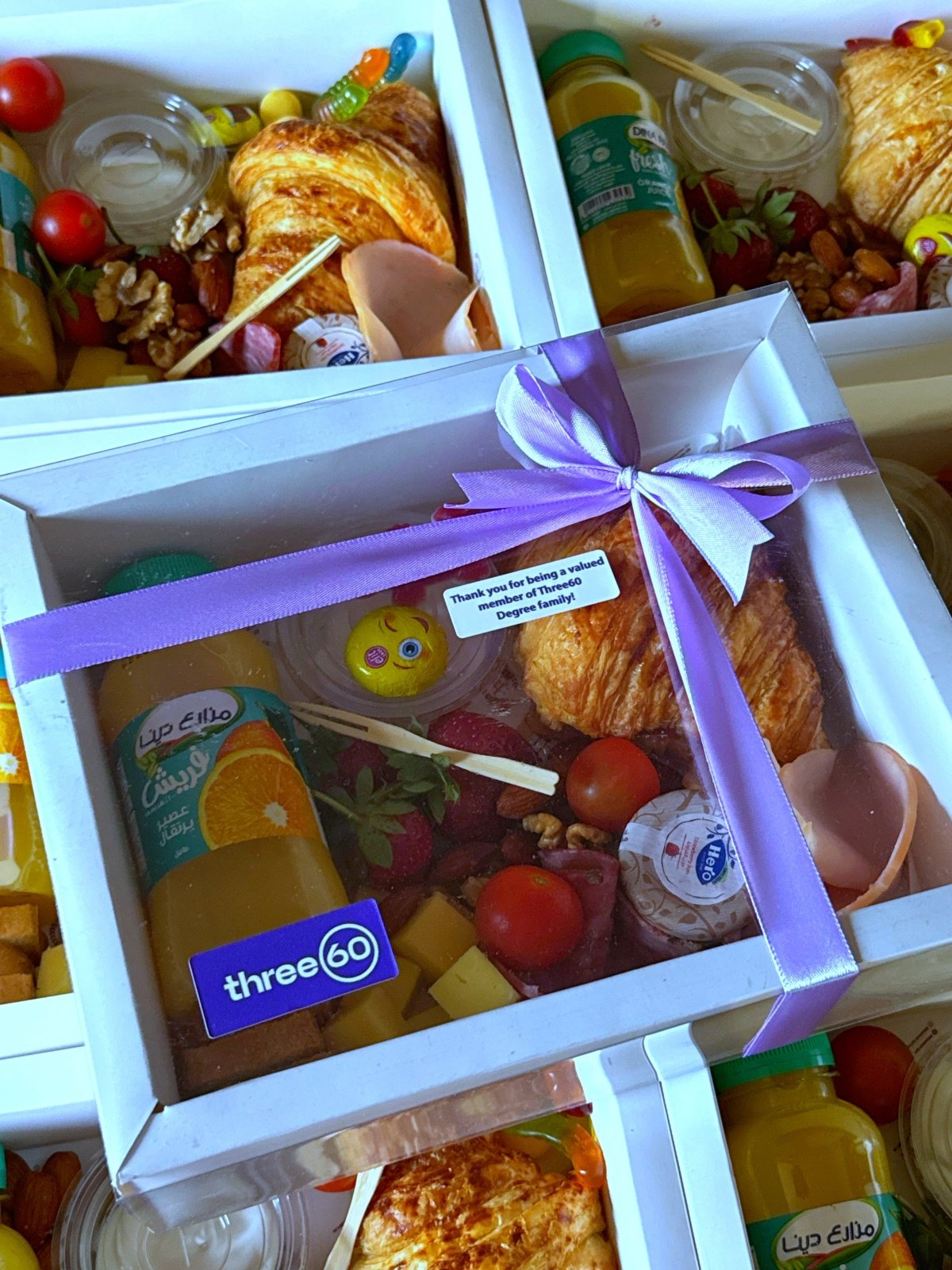 Multiple Team Fuel Boxes with purple ribbons, arranged for corporate distribution, each containing a well-balanced breakfast selection and Three60 thank-you label.
