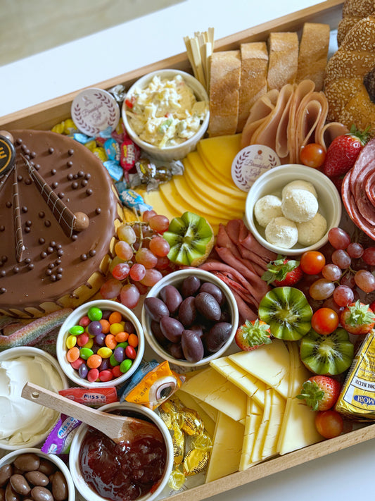 Angled view of The Celebration Tray showing sesame bread rings, croissants, cheeses, and fresh fruits.