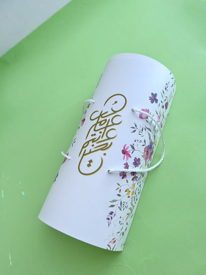 The Grand Kahk Box – Closed floral cylinder gift box, top view showing gold Arabic calligraphy and rope handle