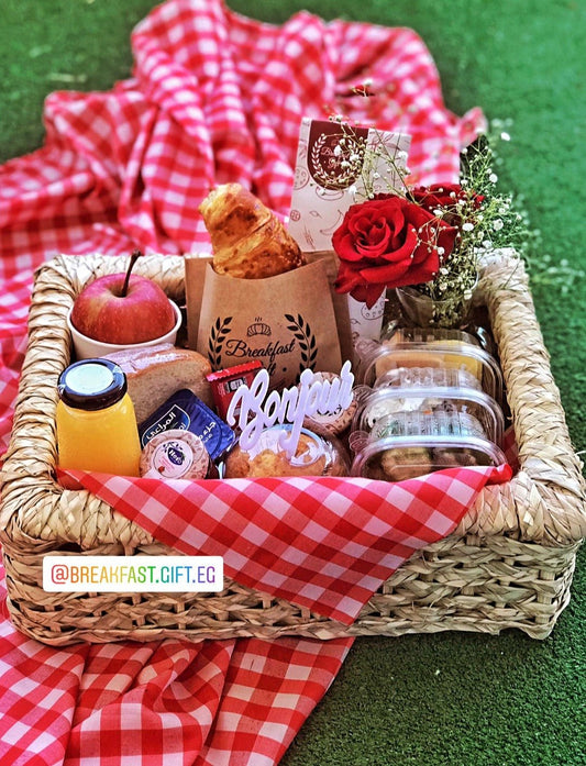 Breakfast Basket & Vase Flowers gift set, featuring a wicker tray with a flaky croissant, toast, muffin cake, fresh fruit, natural juice, cheese, honey, jam, Kit Kat chocolate, and a 'Bonjour' topper. Includes a vase of fresh red flowers for a beautiful and thoughtful morning surprise.